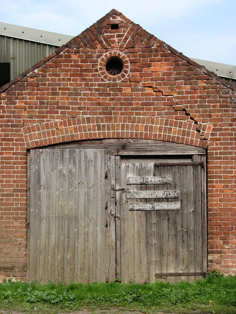 A red-brick barn gable above timber doors, with a stepped crack descending towards the right-hand side of the brick arch.