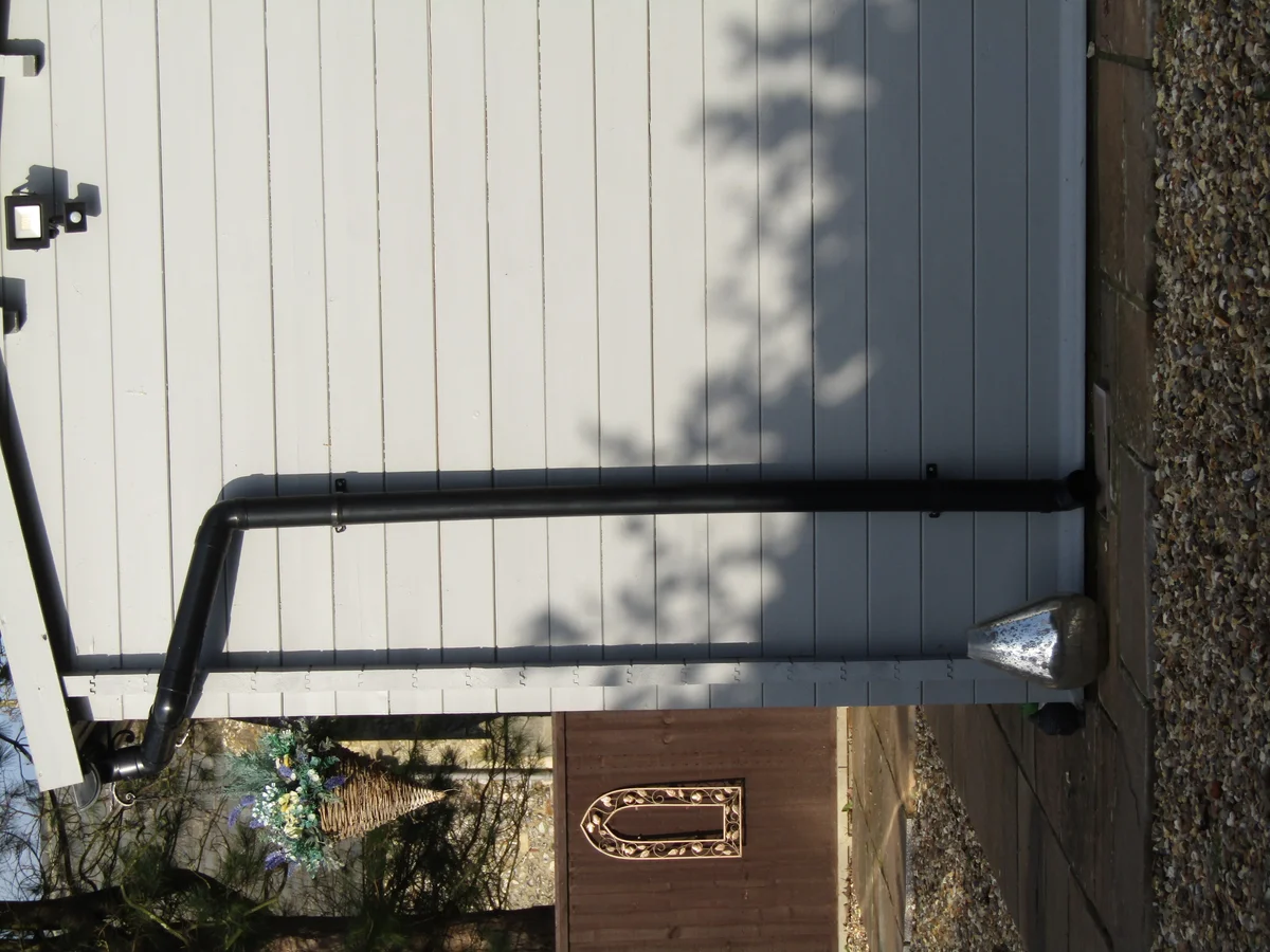 Black gutter connection, offset bends and bracketed downpipe on a timber-clad shed in Trimingham, Norfolk.