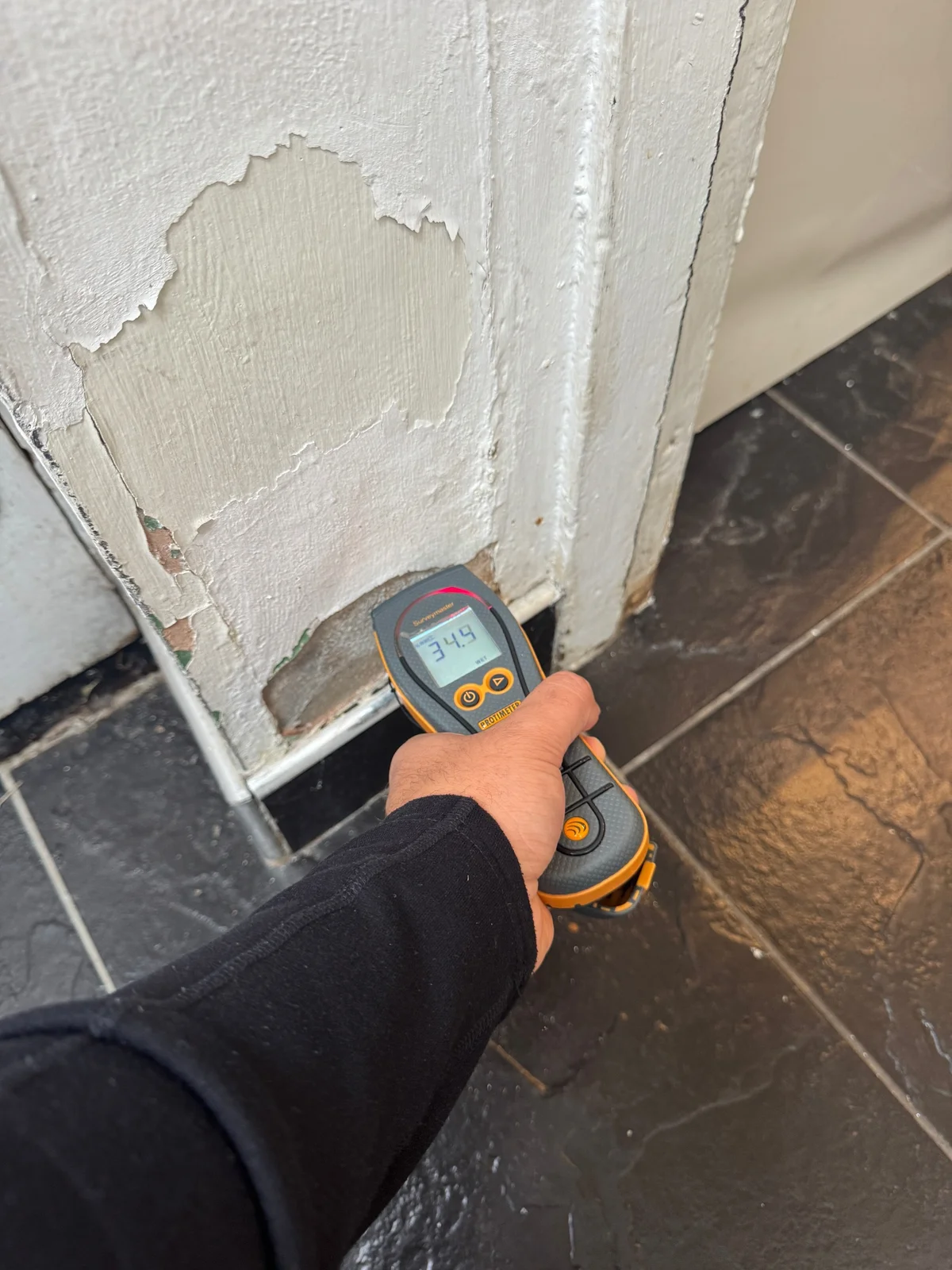 A moisture meter used beside peeling paint and damaged wall decoration.