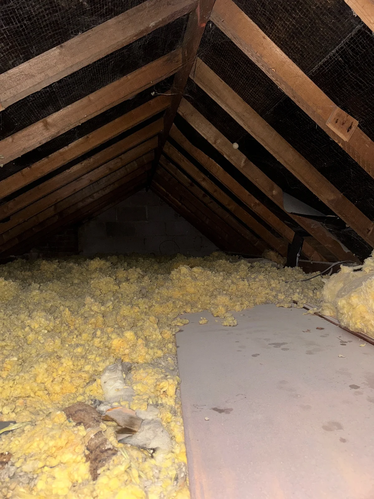 Roof timbers, masonry and unevenly laid insulation seen during a roof-space inspection.