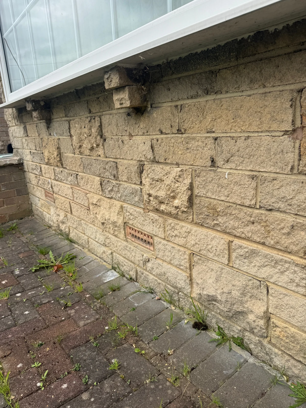 Cracking and open joints in stone masonry beneath a window sill.