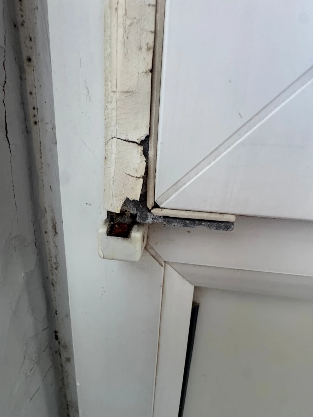A cracked and broken light-coloured hinge cover beside a white external door leaf and frame.