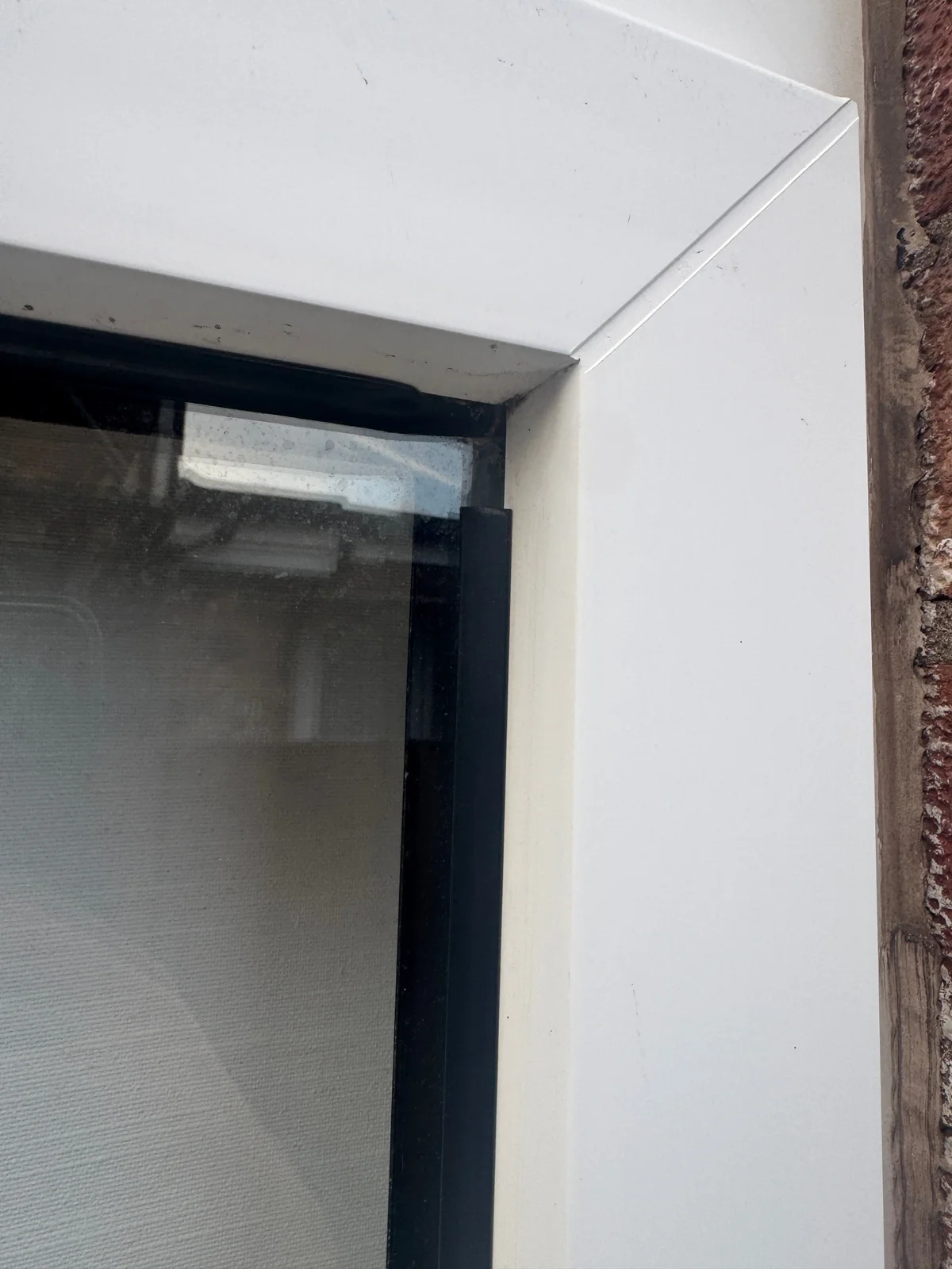 A black glazing gasket has pulled back from the corner of a white window frame, leaving a visible gap.